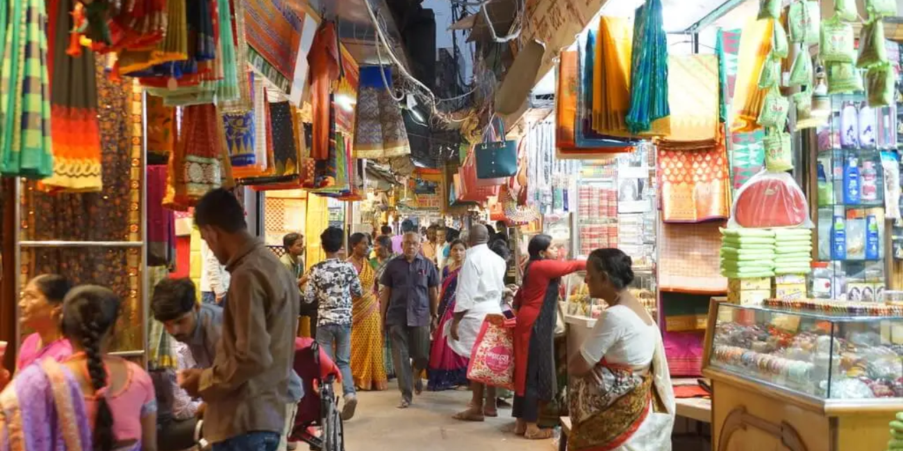 A bustling market scene filled with vibrant cloths hanging from the ceiling, showcasing a variety of colors and patterns.