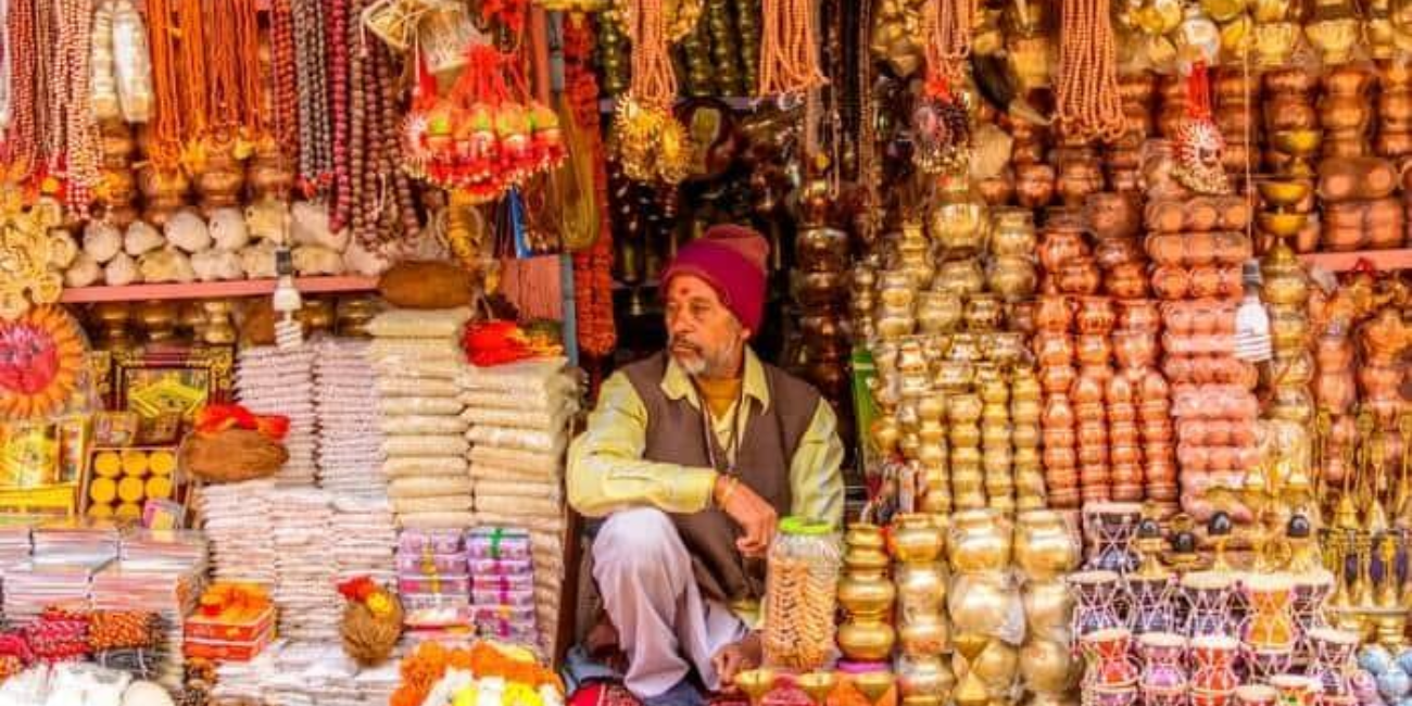 A man sits outside a bead shop, surrounded by colorful beads displayed in the window.