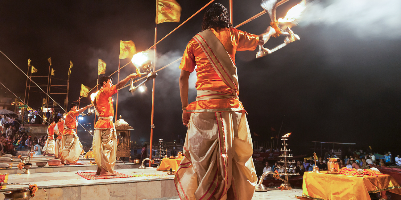 Several performers dance together on stage, displaying synchronized movements and vibrant outfits in a lively performance at ganga aarti.